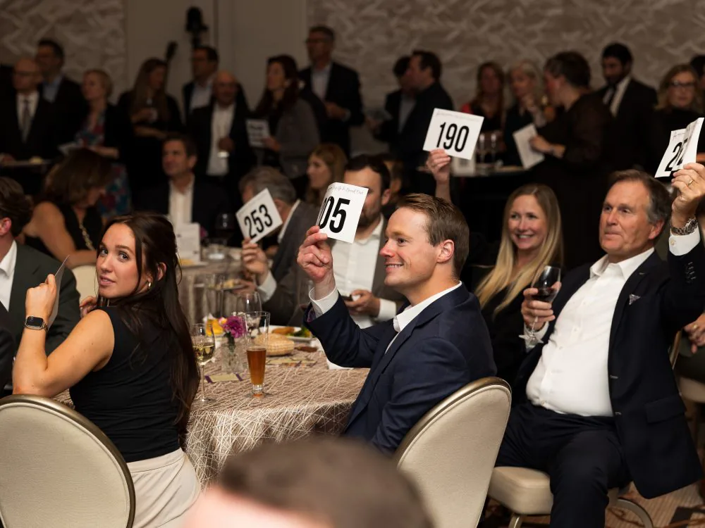 Smiling guests holding up numbered bid cards at a fundraising dinner