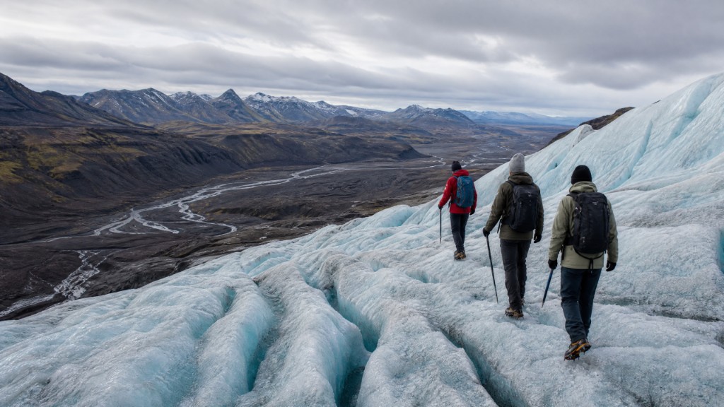 Hikers trekking across a blue-white glacier above a volcanic valley